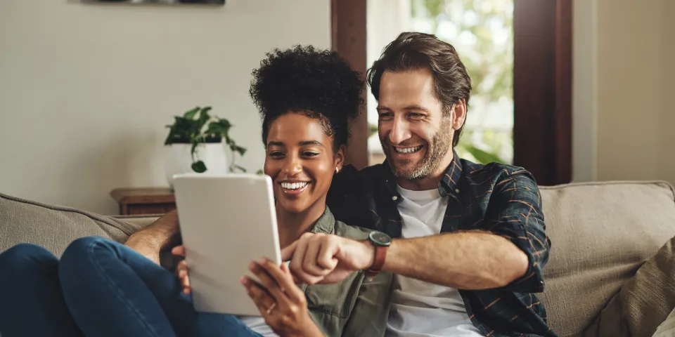 happy young couple using a digital tablet while relaxing on a couch in their living room at home