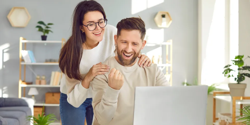 Cheerful young couple using laptop computer at home